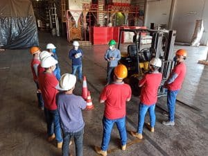 people standing round in a warehouse being trained on using a forklift truck safely 